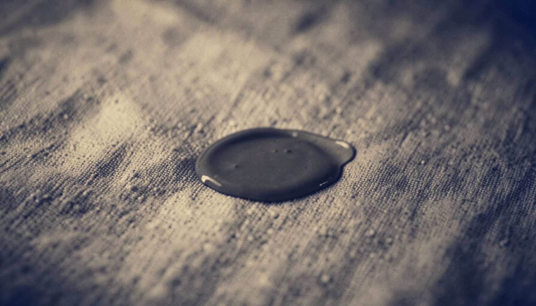 A duotone photograph of a small makeup spill on a textured fabric surface, soft amber and charcoal tones, calm domestic scene.
